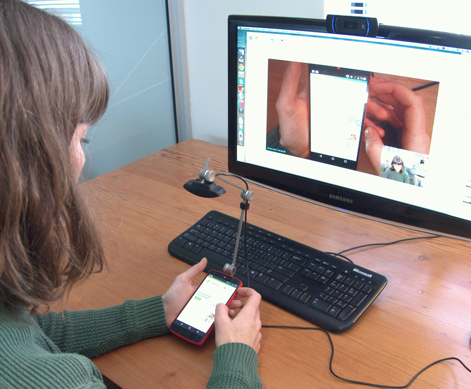 Woman conducting usability testing A woman conducts usability testing on a mobile phone with a camera rig attached to it which shows her phone screen on a computer monitor in the background